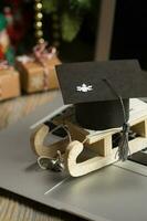 Small wooden sleigh with graduate cap on it placed on a laptop. photo
