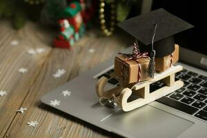 Small wooden sleigh with graduate cap on it placed on a laptop. photo