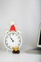 Vintage alarm clock with Santa Claus hat placed close to the laptop. photo