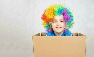 Boy of five years dressed in the costume of a clown stays in a carton paper box. photo