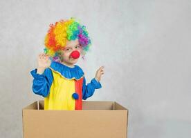 Boy of five years dressed in the costume of a clown stays in a carton paper box. photo