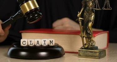 Word CLAIM composed of wooden dices. Wooden gavel and statue of Themis in the background. photo