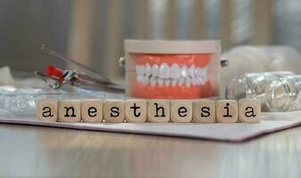 Word ANESTHESIA composed of wooden dices. Pills, documents, pen, human jaw model in the background. photo