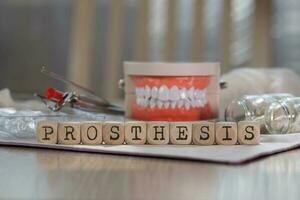 Word PROSTHESIS composed of wooden dices. Pills, documents, pen, human jaw model in the background. photo