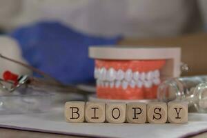 Word BIOPSY composed of wooden dices. Pills, documents, pen, human jaw model in the background. photo