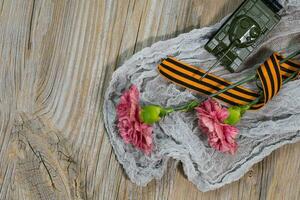 Two pink carnations, Saint George ribbon and military tank on a wooden surface. photo