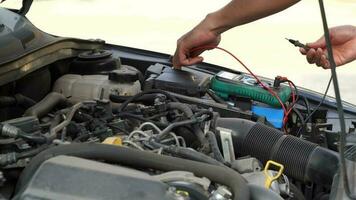 technicien chèques le batterie en utilisant une voltmètre capacité testeur, automatique mécanicien les usages une multimètre voltmètre à vérifier le Tension niveau dans une voiture batterie video