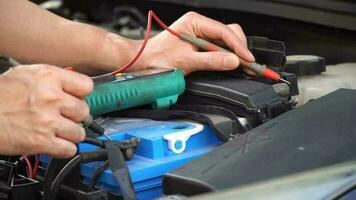 technicien chèques le batterie en utilisant une voltmètre capacité testeur, automatique mécanicien les usages une multimètre voltmètre à vérifier le Tension niveau dans une voiture batterie video