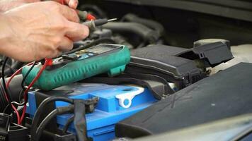 technicien chèques le batterie en utilisant une voltmètre capacité testeur, automatique mécanicien les usages une multimètre voltmètre à vérifier le Tension niveau dans une voiture batterie video