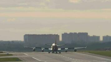 Cinematic footage of a heavy wide body aircraft decelerating after landing, rear view. Flaps up when decelerating. Sunset or dawn on the airfield. Tourism and travel concept video