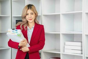 Portrait of a woman business owner showing a happy smiling face as he has successfully invested in her business using computers and financial budget documents at work. photo