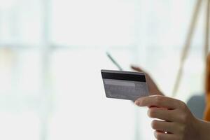 Young adult Asian female consumer holding credit card and smartphone sitting on the floor at home doing online banking transactions. E-commerce virtual shopping, secure mobile banking concept. photo