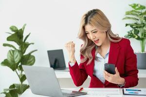 hermosa joven adolescente asiático mujer de negocios utilizando computadora ordenador portátil con manos arriba en ganador es un gesto, contento a ser exitosamente celebrando logro éxito. foto