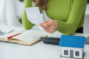 oung Asian woman sitting and calculating expenses and mortgage with calculator and house on table Worried about payments and non-repayable loans, business, and property photo