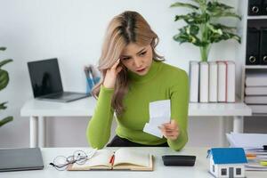 oung Asian woman sitting and calculating expenses and mortgage with calculator and house on table Worried about payments and non-repayable loans, business, and property photo