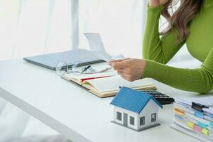 oung Asian woman sitting and calculating expenses and mortgage with calculator and house on table Worried about payments and non-repayable loans, business, and property photo