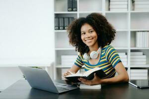 Female students note from the books at the African girl library sitting at the desk using laptop computer and tablet to search an online informations. photo