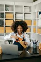 Startup small business SME, Entrepreneur owner African woman using smartphone or tablet taking receive and checking online purchase shopping order to preparing pack product box. photo