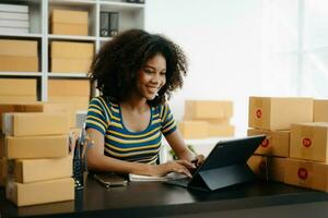 Small business entrepreneur SME freelance African woman working at home office, BOX,tablet and laptop online, marketing, packaging, delivery,  e-commerce concept photo