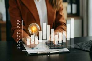 Businesswoman holding and putting lightbulb on coins stack on table for saving energy and money conceptIdea saving energy and accounting finance photo