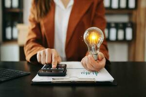 mujer de negocios participación y poniendo bombilla en monedas apilar en mesa para ahorro energía y dinero conceptoidea ahorro energía y contabilidad Finanzas foto