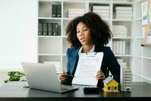 Young real estate agent worker working with laptop and tablet at table in office and small house beside it. photo