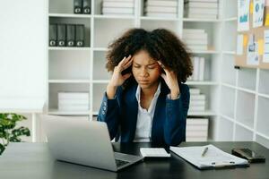 Overworked young African businesswoman office worker suffering from neck pain after had a long day at her office table. office syndrome concept photo