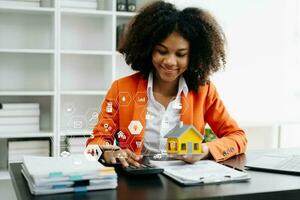 Young real estate agent worker working with laptop and tablet at table in office and small house beside it. photo