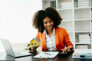 Young real estate agent worker working with laptop and tablet at table in office and small house beside it. photo