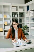 asiático mujer de negocios trabajando en el oficina con trabajando bloc, tableta y ordenador portátil documentos en oficina foto