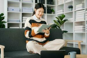 Confident Asian woman with a smile standing holding notepad and tablet in living room on the sofa at home photo