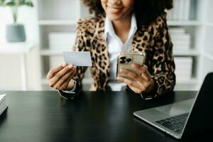 African Woman using smart phone for mobile payments online shopping,omni channel,sitting on table,virtual icons graphics interface screen photo