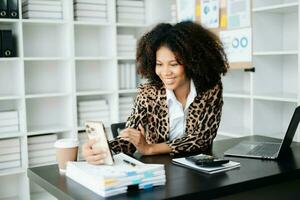 Young African woman typing on tablet and laptop while sitting at the working black table office photo