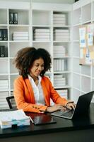 Young African woman typing on tablet and laptop while sitting at the working black table office photo