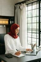 Young Arabic female entrepreneur wearing a hijab working online with a laptop at office photo