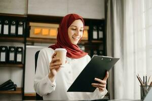 Young Arabic female entrepreneur wearing a hijab working online with a laptop at office photo