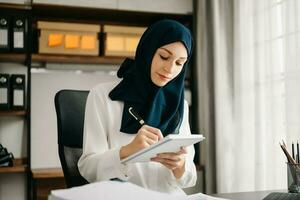 Young Muslim woman working with laptop and tablet  in her modern business home office. photo