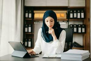 joven musulmán mujer trabajando con ordenador portátil y tableta en su moderno negocio hogar oficina. foto