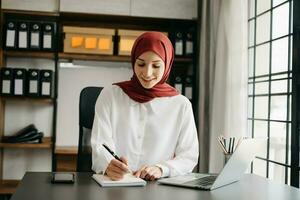 Young Arabic female entrepreneur wearing a hijab working online with a laptop at office photo