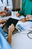 Medical team having a meeting with doctors in white lab coats and surgical scrubs seated at a table discussing a patients working online using computers photo