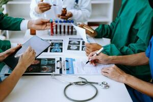 Medical team having a meeting with doctors in white lab coats and surgical scrubs seated at a table discussing a patients working online using computers photo