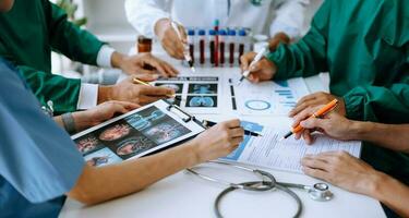 Medical team having a meeting with doctors in white lab coats and surgical scrubs seated at a table discussing a patients working online using computers photo