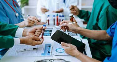 Medical team having a meeting with doctors in white lab coats and surgical scrubs seated at a table discussing a patients working online using computers photo