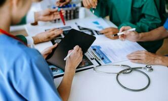Medical team having a meeting with doctors in white lab coats and surgical scrubs seated at a table discussing a patients working online using computers photo