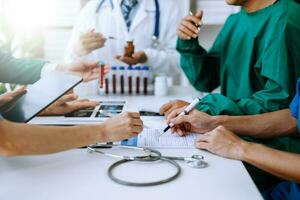 Medical team having a meeting with doctors in white lab coats and surgical scrubs seated at a table discussing a patients working online using computers photo