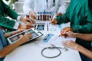 Medical team having a meeting with doctors in white lab coats and surgical scrubs seated at a table discussing a patients working online using computers photo