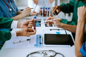 Medical team having a meeting with doctors in white lab coats and surgical scrubs seated at a table discussing a patients working online using computers photo
