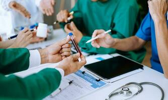 Medical team having a meeting with doctors in white lab coats and surgical scrubs seated at a table discussing a patients working online using computers photo