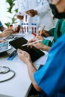 Medical team having a meeting with doctors in white lab coats and surgical scrubs seated at a table discussing a patients working online using computers photo