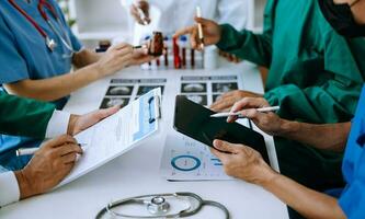 Medical team having a meeting with doctors in white lab coats and surgical scrubs seated at a table discussing a patients working online using computers photo